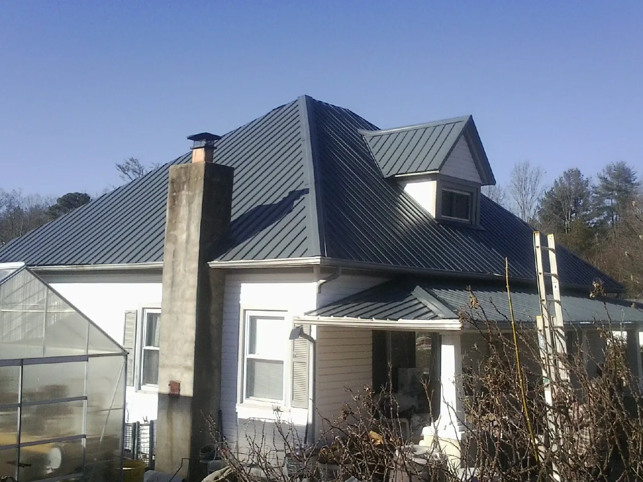 Dark blue standing seam metal roof on a white farmhouse with dormer — Slate & Tile Roof Repair by Roofing Brothers in Jennings