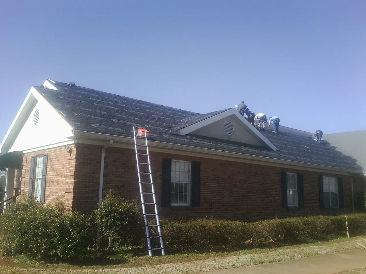 Crew tearing shingles off a brick ranch roof with a ladder set — Emergency Roof Repair work by our crew in Jennings