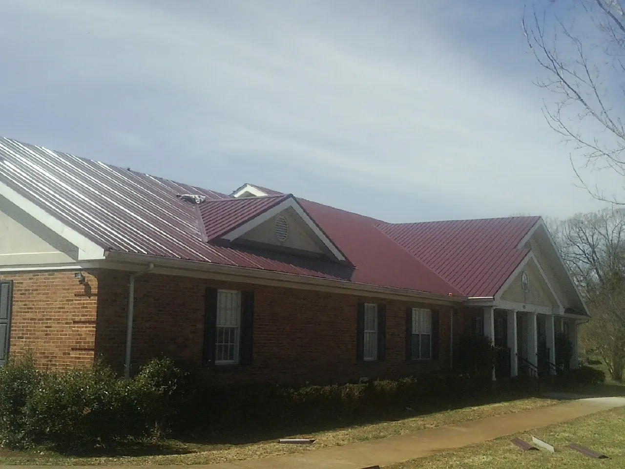 Red metal roof with gabled entries on a long brick building, from a Hail Damage Roof Repair job in Jennings