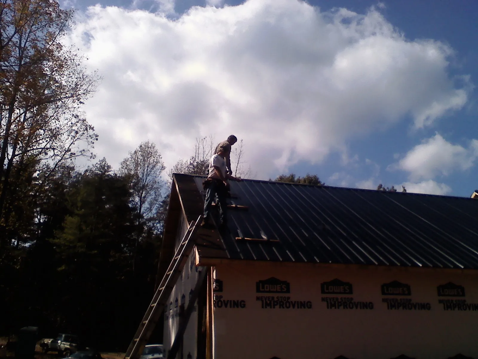 Roofer fastening dark metal panels high against a cloudy sky, from a Roof Inspection job in Jennings