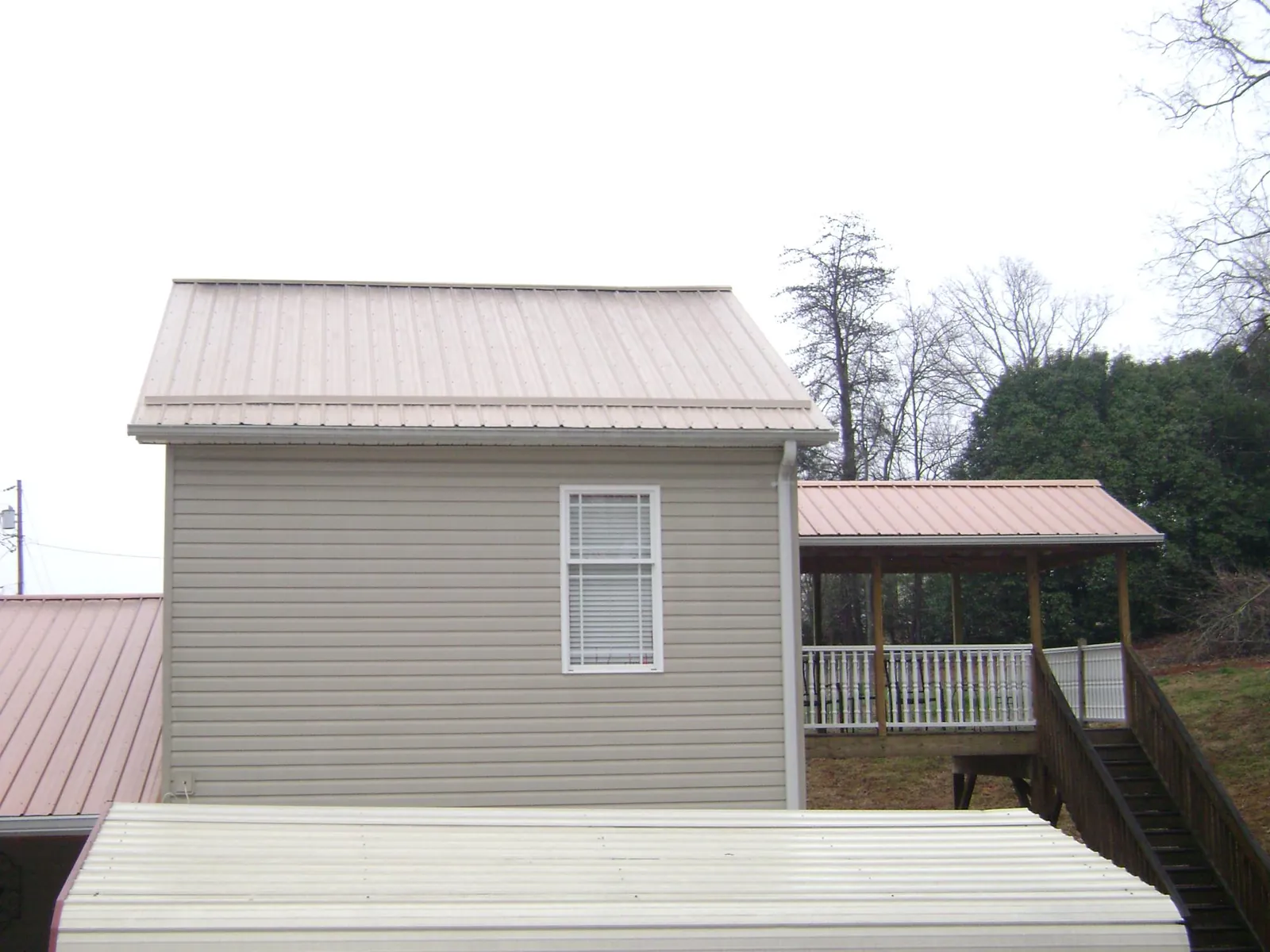 Tan metal roofs on a two story addition and attached porch, from a Roof Replacement job in Jennings